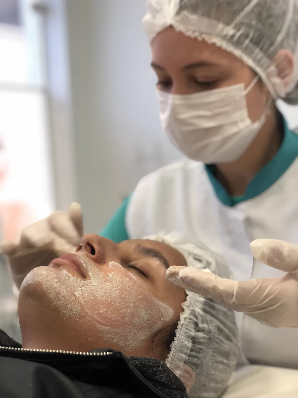 Esteticista de touca, máscara e luvas fazendo limpeza de pele em cliente na Ergon Saúde, em Sorocaba