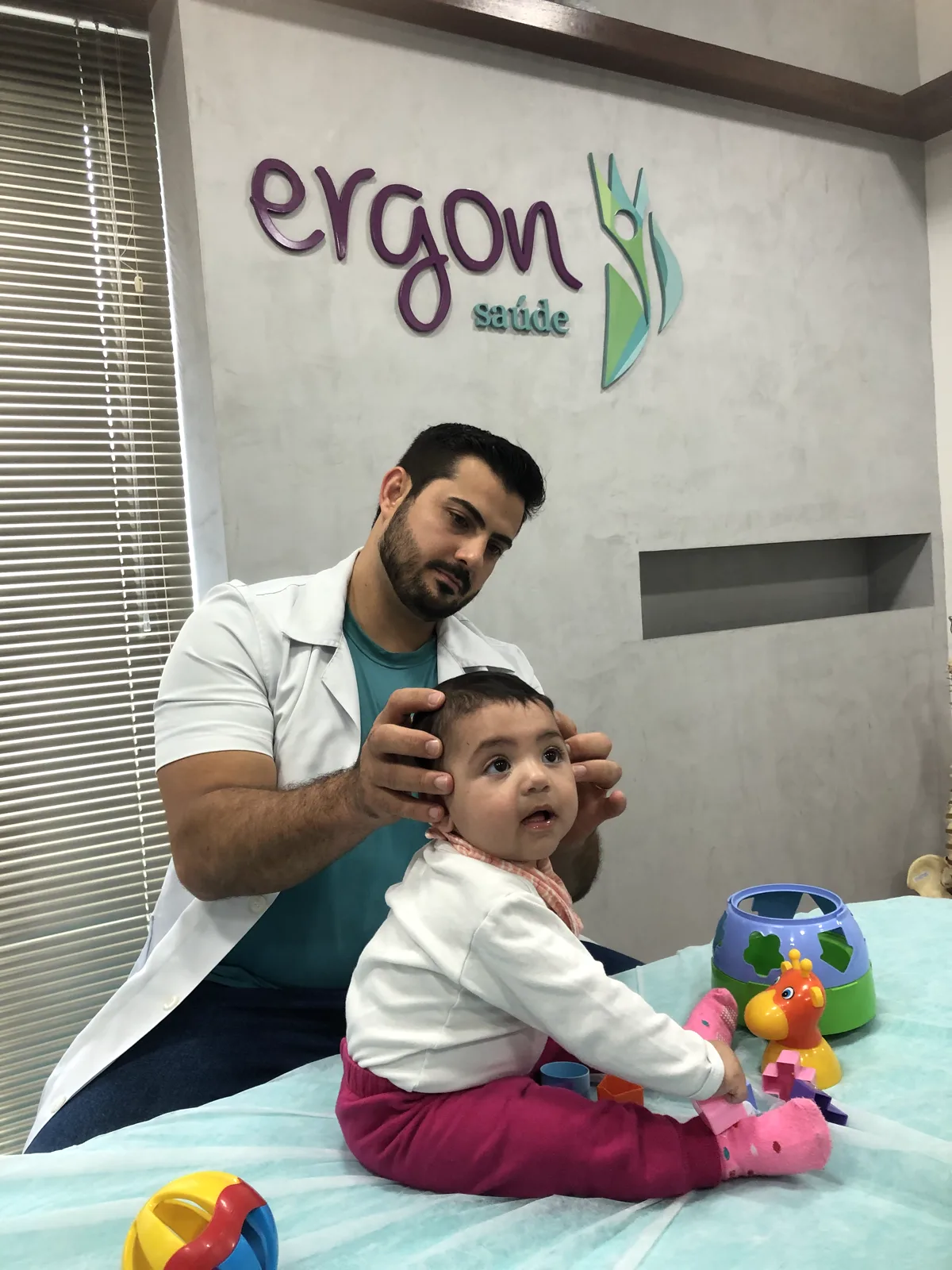Fisioterapeuta da Ergon atendendo um bebê sentado na maca, na osteopatia pediátrica em Sorocaba