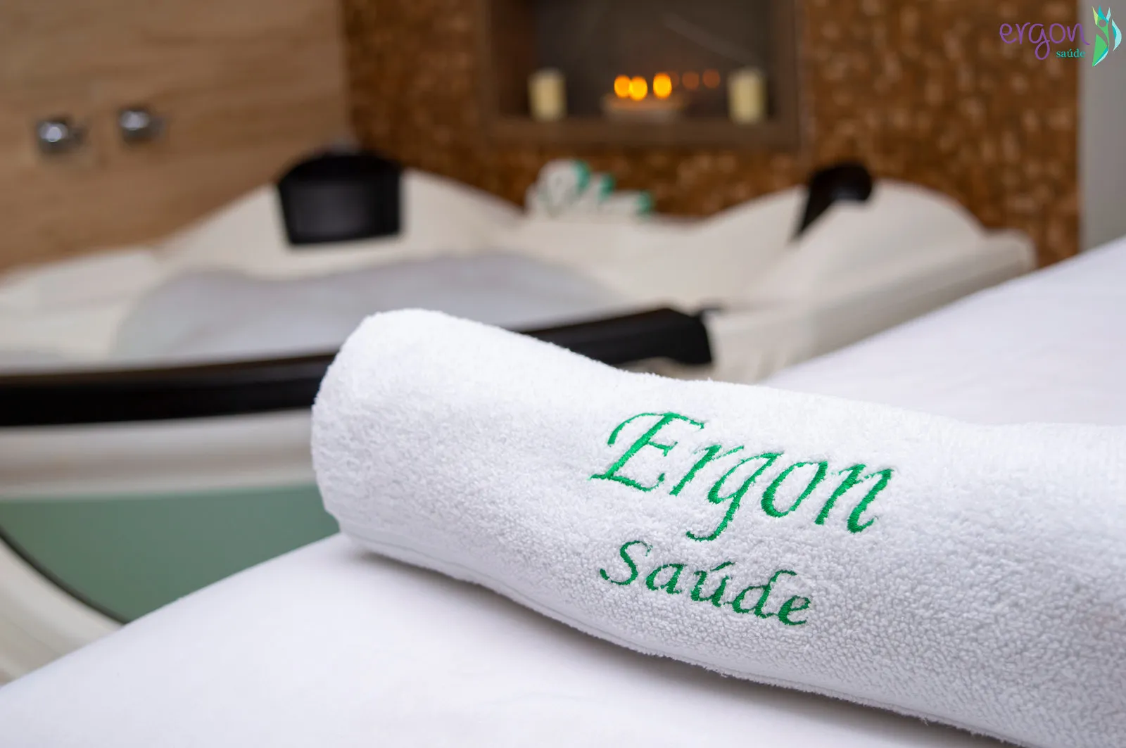 Toalha bordada Ergon Saúde e velas acesas na sala de spa onde é feita a massagem com velas em Sorocaba
